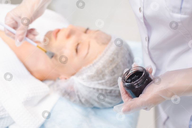 Скачать Руки косметолога, наносящего углеродный наногель на лицо молодой пациентки с помощью кисточки, готовящейся к процедурам карбонового пилинга фотосток Ozero