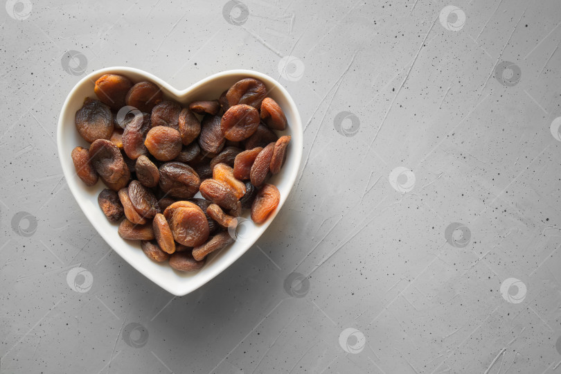 Скачать Сушеные органические абрикосы в тарелке в форме сердца на фоне серого бетона. фотосток Ozero