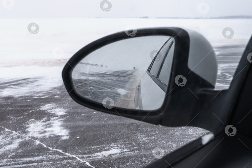 Скачать Вид из зеркала заднего вида автомобиля во время снегопада и метели, дорога частично покрыта снегом фотосток Ozero