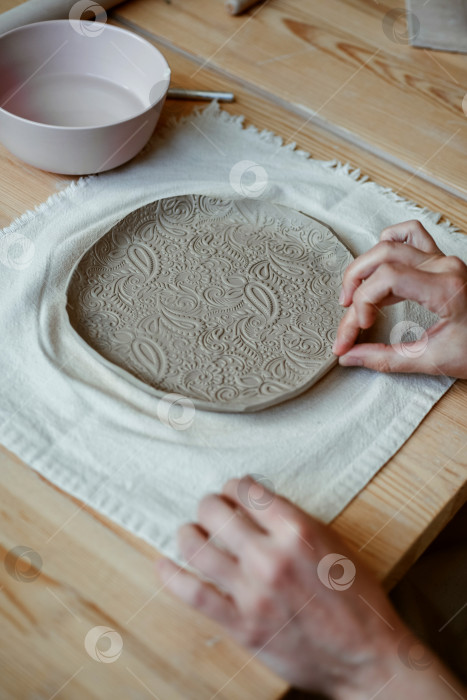 Скачать Красивая тарелка из необработанной глины с орнаментом на столе в мастерской фотосток Ozero