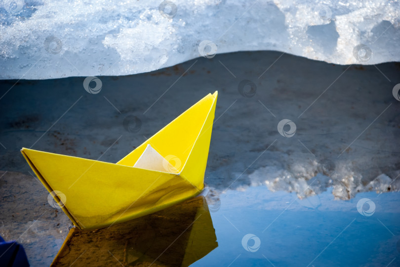 Скачать По озеру плывет разноцветный бумажный кораблик. Вокруг него лед и снег. фотосток Ozero