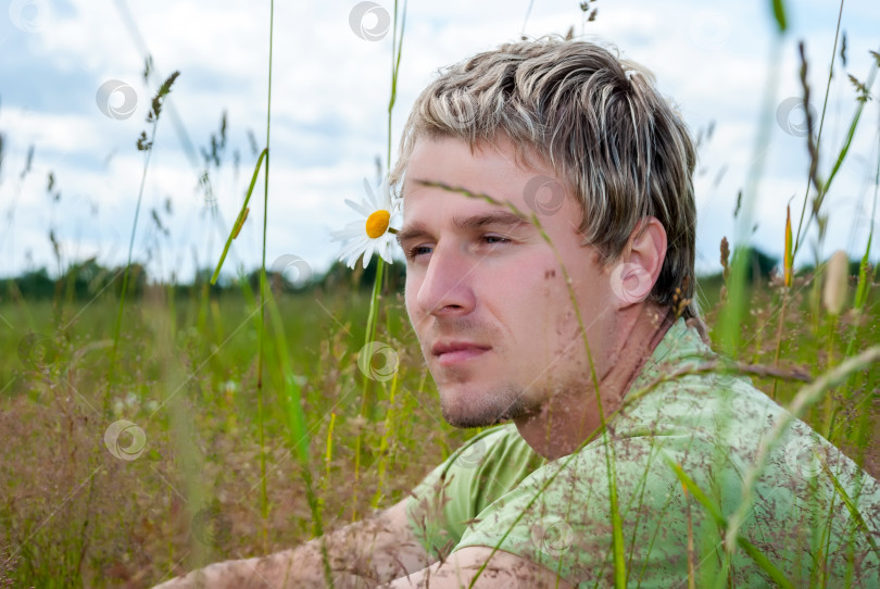 Скачать Красивый мужчина в зеленой футболке сидит на поле в высокой траве. фотосток Ozero