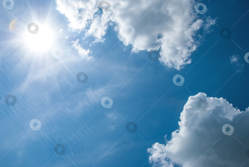 Скачать Воздушные белые облака, солнце с длинными лучами и бликами на голубом небе. Небесный пейзаж фотосток Ozero