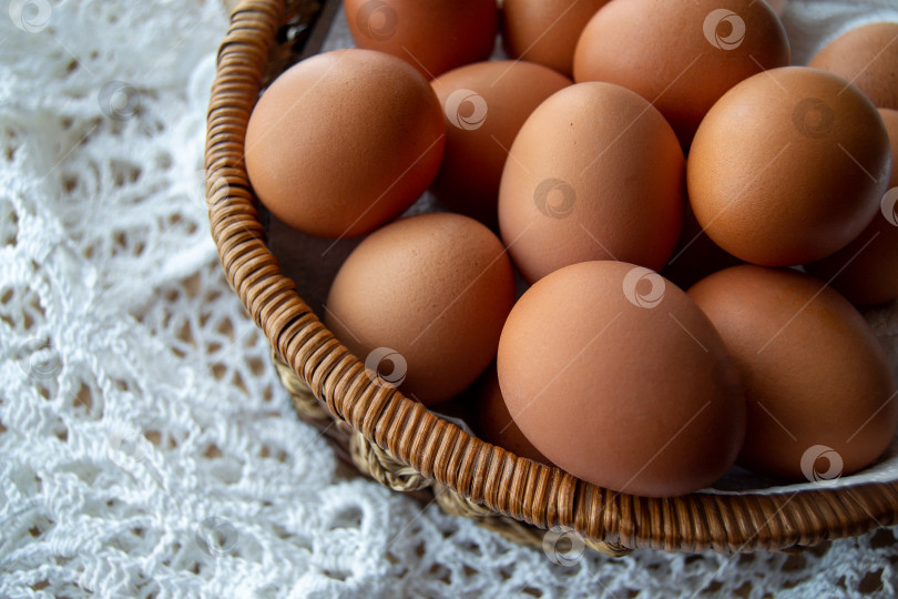 Скачать Куриные яйца лежат в плетеной корзинке, которая стоит на столе, на белой кружевной скатерти. фотосток Ozero