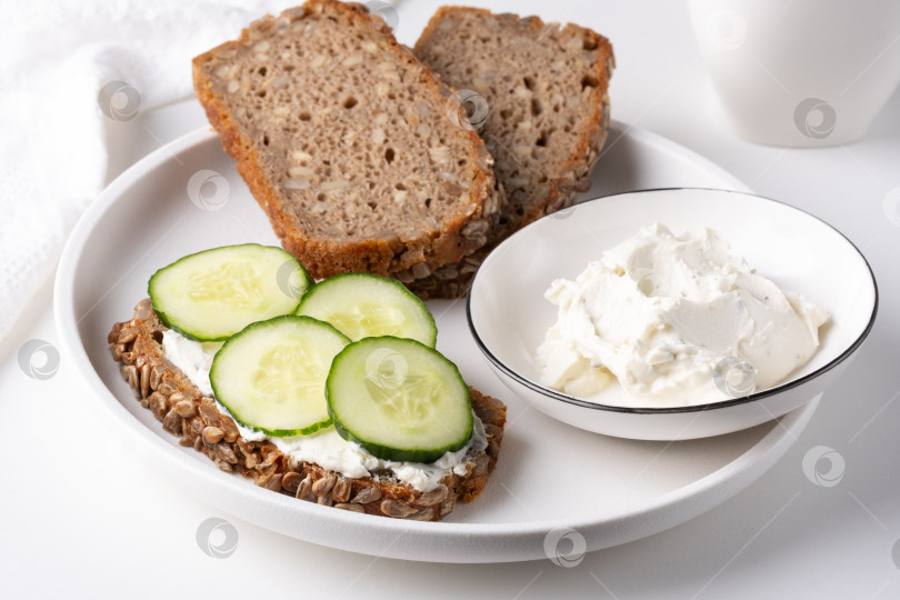 Скачать Ржаной хлеб со сливочным сыром и огурцами на белом столе. Ржаной хлеб из цельного зерна с семечками фотосток Ozero