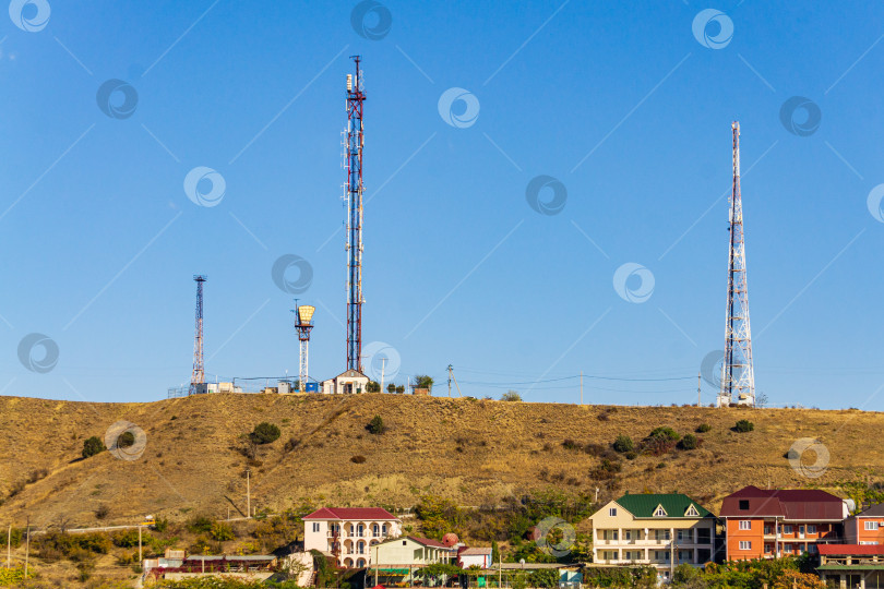 Скачать Вид из окна отеля на телекоммуникационные вышки, расположенные на вершинах Крымского хребта. На переднем плане - жилые здания, окруженные деревьями. фотосток Ozero