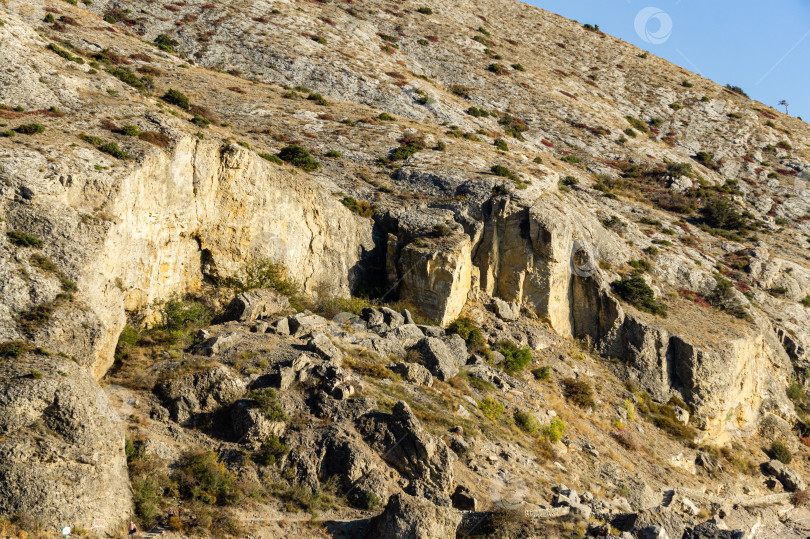 Скачать Мыс Алчак на южном побережье Крыма на окраине курортного города Судак. Потрясающий вид на большую гору с гротом Эоловой арфы на тропе Алчак-Кая. Крупный план огромных камней и природных валунов фотосток Ozero