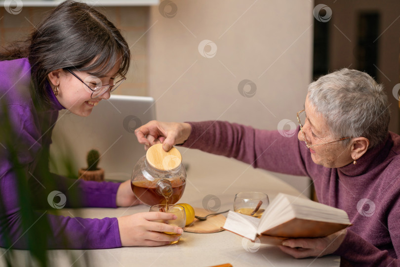 Скачать бабушка и внучка пьют чай, сидя за столом, и читают книгу фотосток Ozero