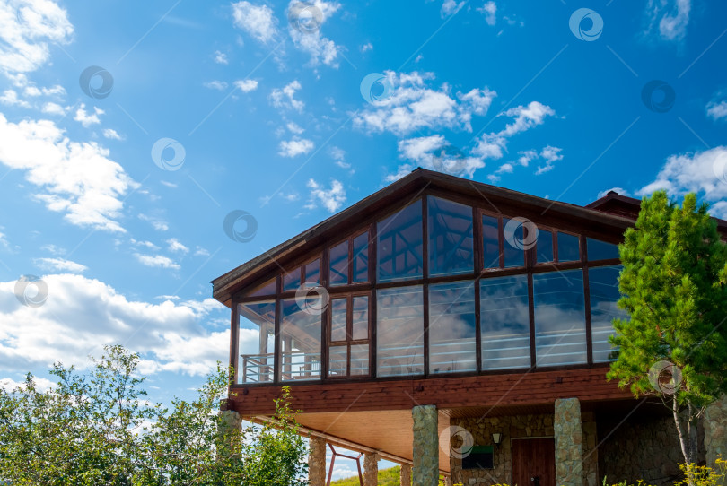 Скачать Красивый коттедж со стеклянным фасадом на фоне голубого неба и деревьев. фотосток Ozero