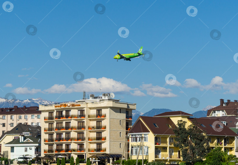 Скачать Airbus A320-271N совершает посадку над зданиями на побережье горной реки Мзымта на фоне вершин Кавказских гор. Федеральная территория Сириус в Имеретинской низменности. Адлер Сириус, Россия - 18 мая 2021 г. фотосток Ozero