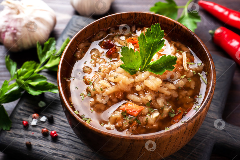 Скачать Вегетарианский суп харчо с рисом и овощами. Чеснок, острый перец, помидоры. Деревянный деревенский фон, тарелки из натурального бамбука. фотосток Ozero