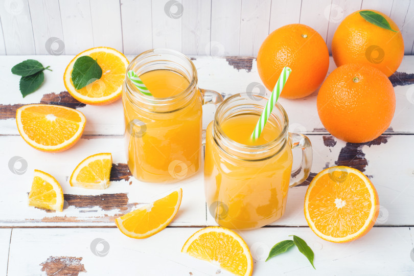Скачать Апельсиновый сок в стеклянных банках и свежие апельсины на фоне белого дерева в деревенском стиле. фотосток Ozero
