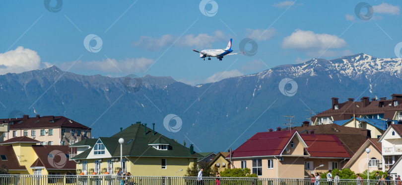 Скачать Boeing 737-900ER Azur Air заходит на посадку в аэропорту Адлера над зданиями на побережье горной реки Мзымта на фоне Кавказских гор. Адлер Сириус, Россия - 18 мая 2021 г. фотосток Ozero