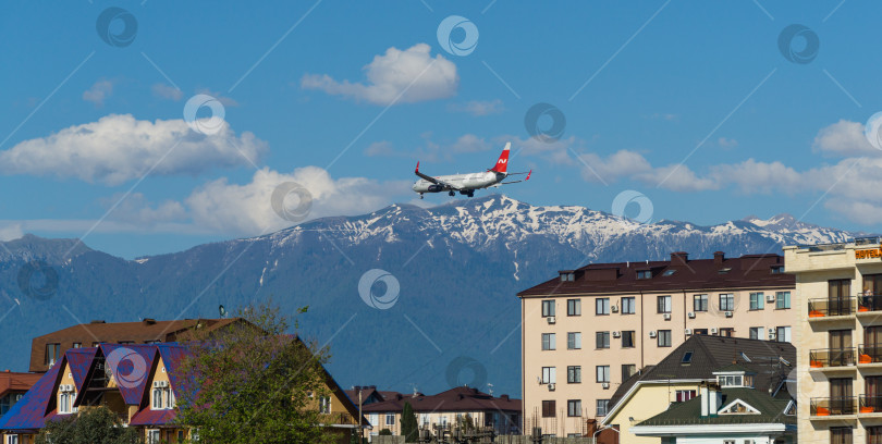 Скачать Boeing 737-900ER заходит на посадку в аэропорту Адлера над зданиями на побережье горной реки Мзымта на фоне Кавказских гор. Адлер Сириус, Россия - 18 мая 2021 г. фотосток Ozero