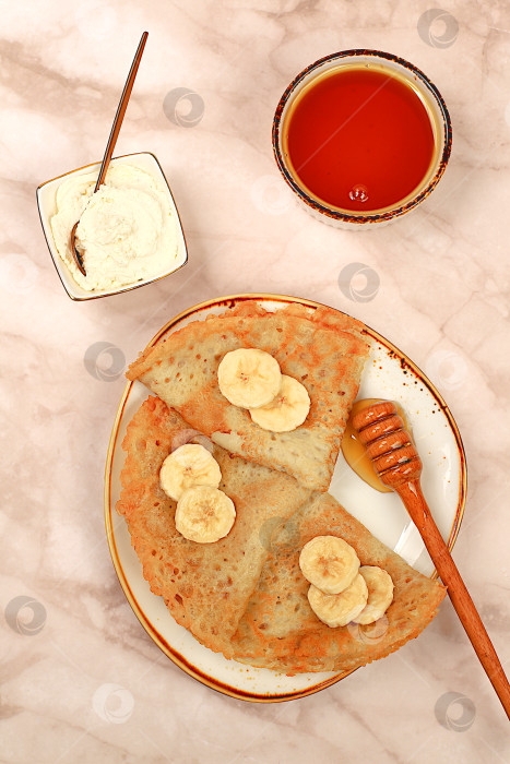 Скачать Вкусные русские блинчики с мягким сыром, бананами и медом на мраморном столе. Полезный завтрак с ингредиентами, концепцией карнавала и традиционной национальной кухней, фотосток Ozero