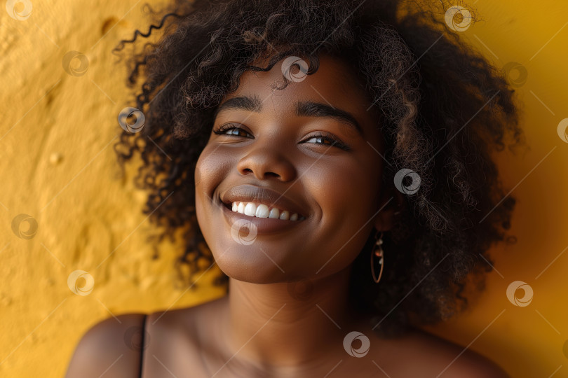 Скачать Портрет симпатичной позитивной молодой афроамериканки с вьющейся прической в стиле афро, стоящей на фоне желтой стены, стиль жизни фотосток Ozero