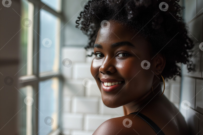 Скачать Портрет красивой позитивной молодой афроамериканки с вьющейся прической в стиле афро, смотрящей в камеру, стоя дома, индивидуальность фотосток Ozero