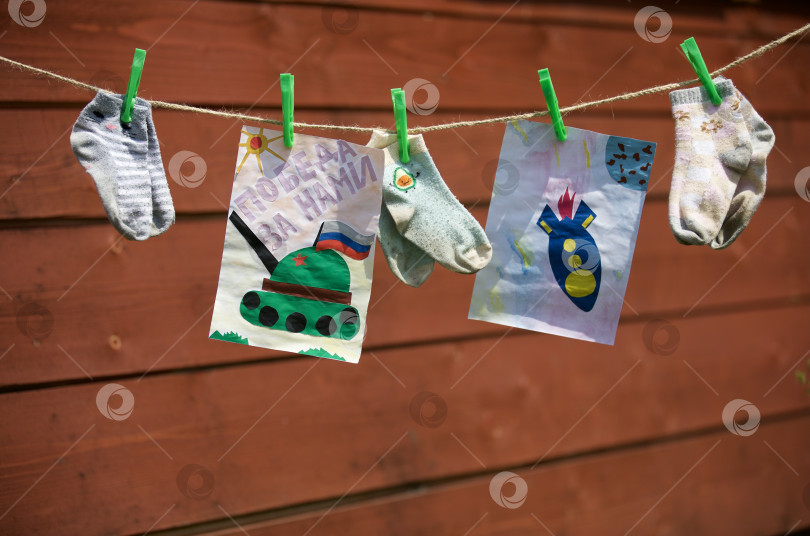 Скачать Детские рисунки, аппликации висят, на бельевой верёвке среди носков фотосток Ozero