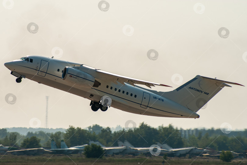 Скачать Украинский двухмоторный реактивный пассажирский самолет Ан-148 взлетает на размытом фоне военных самолетов за взлетно-посадочной полосой. МАКС-2007. Выборочный фокус. МАКС-2007. фотосток Ozero