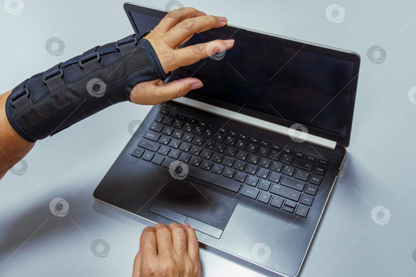 Скачать Женская рука в черном ортезе закрывает компьютер после работы. фотосток Ozero
