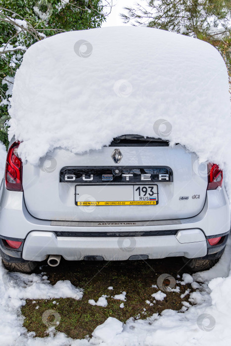 Скачать Приключенческий автомобиль Renault Duster, припаркованный под огромным сугробом. Крупный план. Сугробы на крыше автомобиля после сильного ночного снегопада. Экстремальные снежные заносы на Юге России. фотосток Ozero