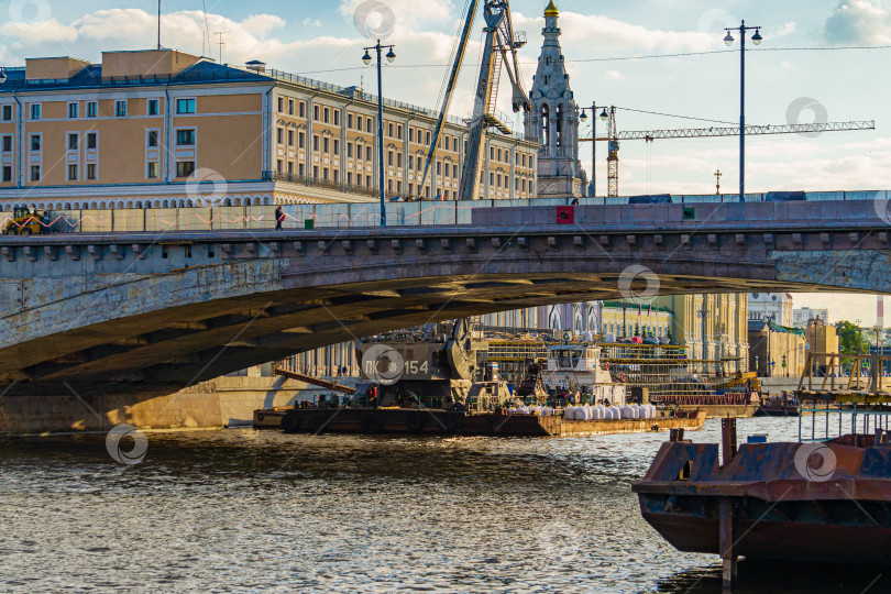 Скачать Москва, Россия - 16 июня 2019 года: Ремонт автомобильного моста на Москворецкой набережной. Ржавая баржа пришвартована к пирсу. За мостом установлен плавучий кран фотосток Ozero