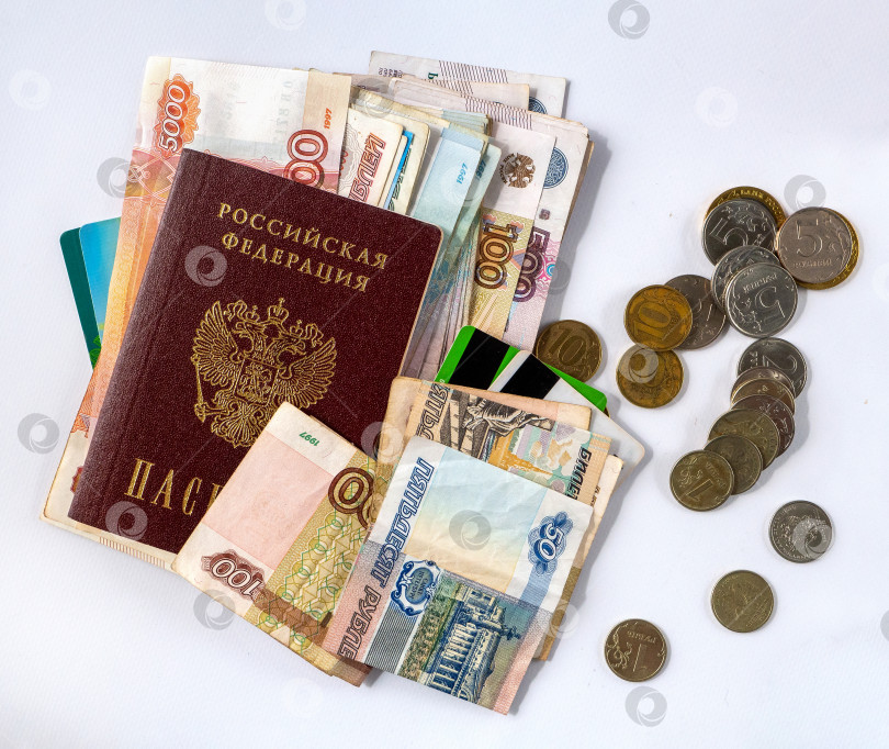Скачать Российские бумажные деньги и рублевые монеты, а также пластиковые карты и паспорт Российской Федерации расположены по диагонали на белом фоне. Деньги расположены хаотично. фотосток Ozero