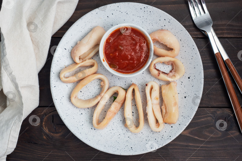 Скачать Обжаренные кольца кальмара с томатным соусом и лимоном. Место для копирования фона из темного дерева. Вид сверху. фотосток Ozero