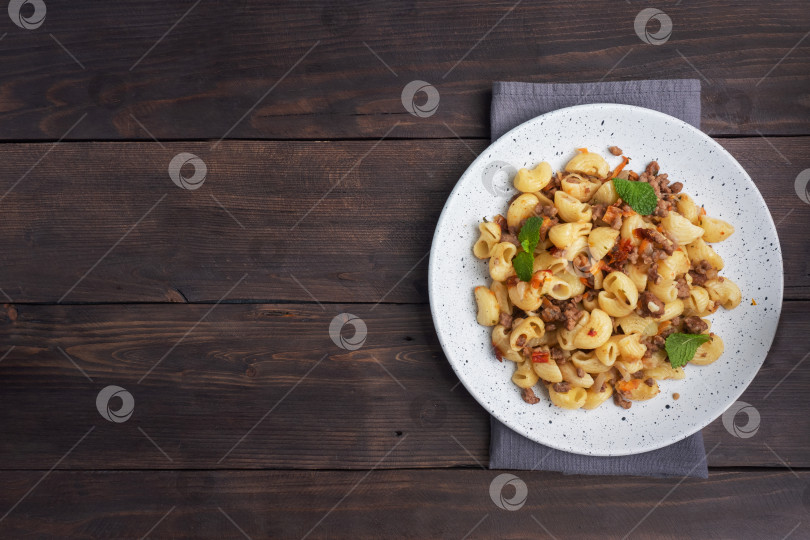 Скачать Тушеные макароны с говяжьим фаршем и овощами, макароны по-флотски на тарелке. Фон из темного дерева. Место для копирования. фотосток Ozero