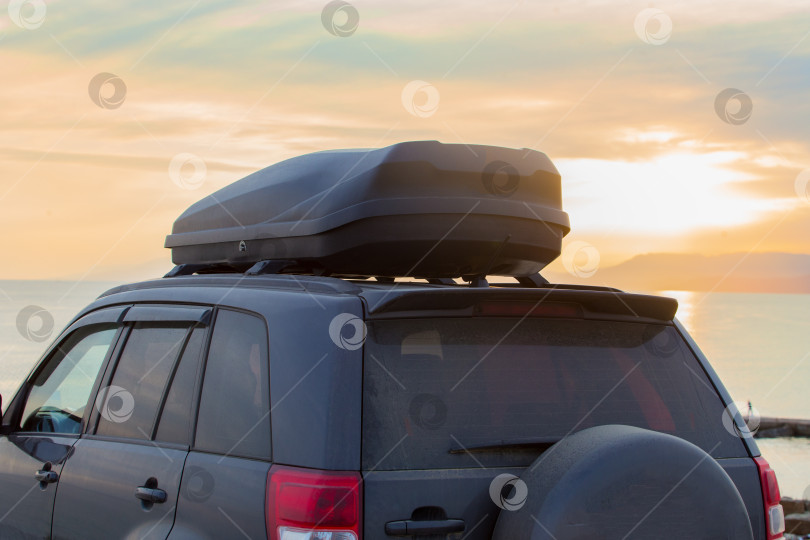 Скачать Внедорожник с автобоксом на крыше на берегу моря на закате. фотосток Ozero