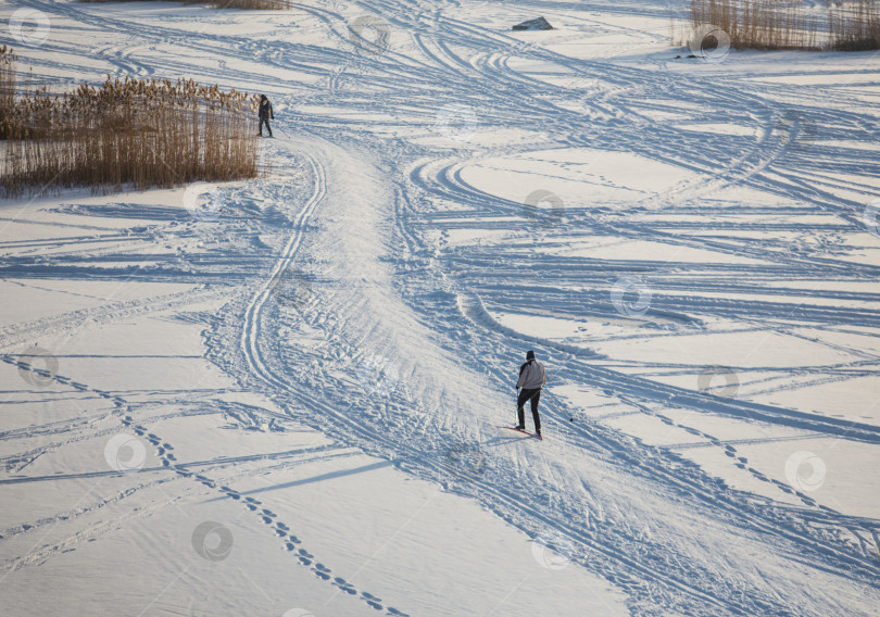Скачать Два лыжника катаются на лыжах по замерзшей поверхности реки фотосток Ozero