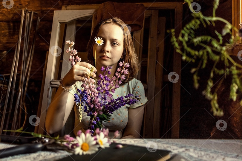 Скачать Молодая красивая девушка в винтажном платье в старом деревенском доме собирает букет люпинов в вазу фотосток Ozero