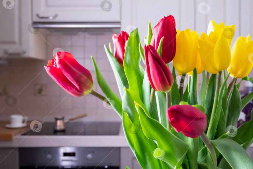 Скачать Букет красивых желтых и красных тюльпанов стоит на столе в уютной кухне. фотосток Ozero