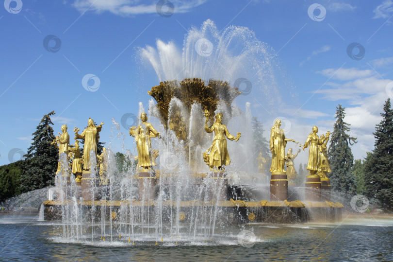 Скачать Фонтан Дружбы народов - главный фонтан на фоне голубого неба. Пятнадцать золотых статуй женщин в центре фонтана. Струи воды падают в огромную чашу. фотосток Ozero