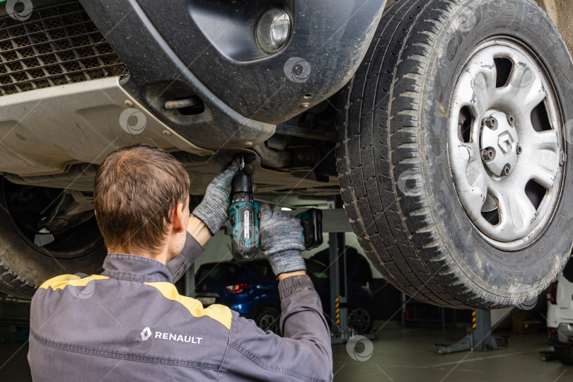 Скачать Техническое обслуживание автомобиля Renault в сервисном центре. Механик снимает защиту картера двигателя автомобиля с помощью специального инструмента. Дилерский центр Renault в Мега Адыгея. фотосток Ozero