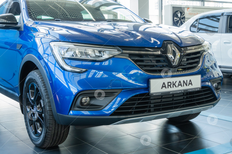 Скачать Синий внедорожник Renault Arkana. Демонстрационный зал в дилерском центре Renault. Крупным планом правая передняя фара, правое переднее колесо и капот. Вид справа сбоку. Мега Адыгея. фотосток Ozero