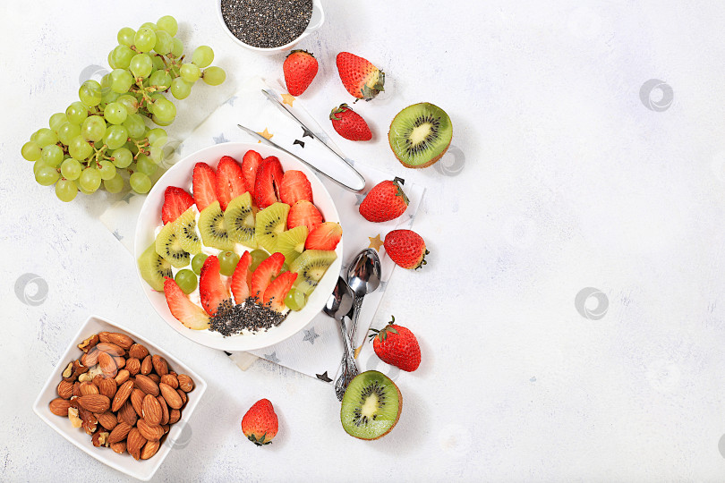 Скачать Полезный завтрак с ингредиентами, дополненный фруктовым салатом с клубникой, киви, мюсли, виноградом, бананом и семенами чиа для похудения. Концепция натурального питания и детокс-диеты фотосток Ozero
