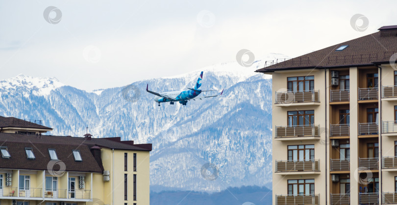 Скачать Boeing 737-800 авиакомпании NordStar совершает полет на фоне заснеженных вершин Кавказских гор и жилых зданий в поселке Сириус напротив Адлера. Сочи, Россия - 16 марта 2021 г. фотосток Ozero