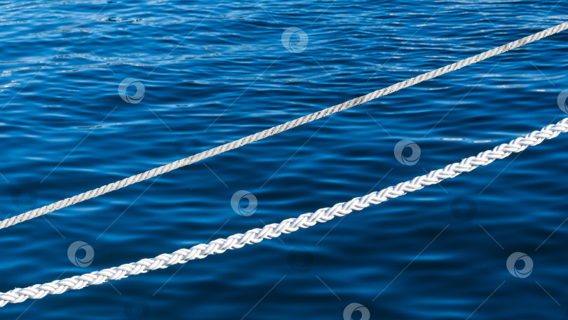 Скачать Белый морской швартовный трос на фоне голубой воды Черного моря. Два белых морских шнура. Фоновое изображение морского белого каната в морском порту Сочи. фотосток Ozero