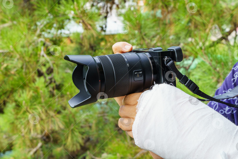 Скачать Фотограф со сломанной рукой в белой гипсовой повязке, держащий фотоаппарат Sony фотосток Ozero