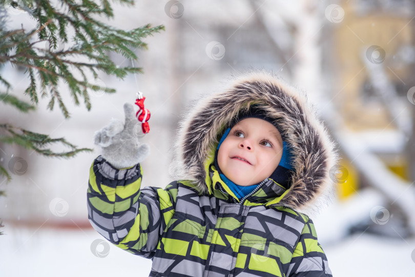 Скачать ребенок осматривает дворовую рождественскую елку на улице снежной зимой фотосток Ozero