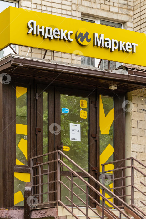 Скачать Логотип Яндекс Маркета на желтом фоне над входом в здание. Логотип интернет-магазина - буква "М" в центре желтого круга. Надпись "Яндекс Маркет" на русском языке. фотосток Ozero
