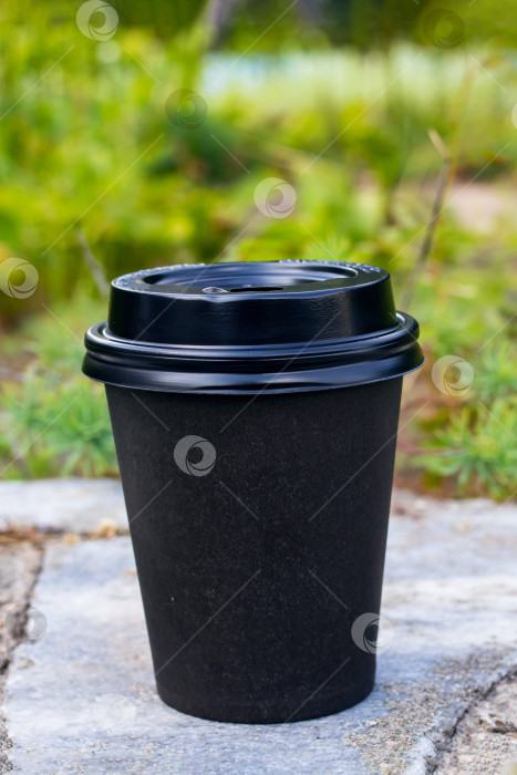 Скачать Черный бумажный стаканчик с кофе на фоне зеленых листьев фотосток Ozero