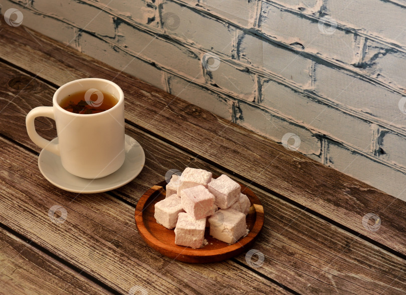 Скачать Чашка горячего травяного чая на блюдце и круглая деревянная тарелка с кучей восточных сладостей в сахарной пудре на деревянном столе. фотосток Ozero