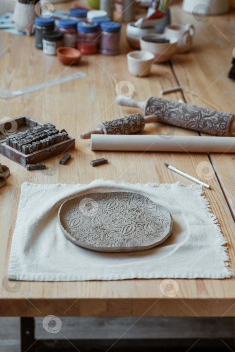 Скачать Красивая тарелка из необработанной глины с орнаментом на столе в мастерской фотосток Ozero
