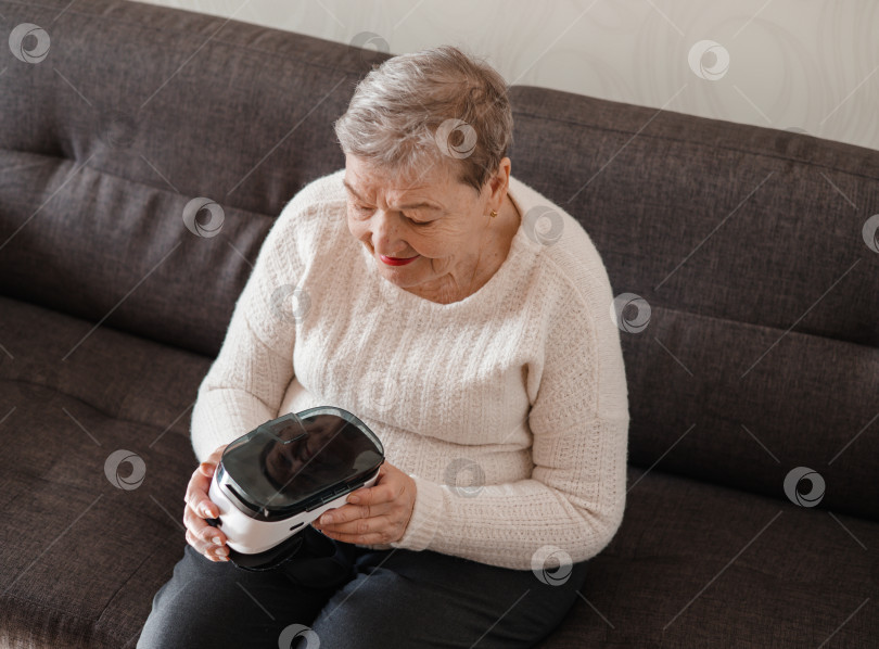 Скачать Пожилая женщина рассматривает очки виртуальной реальности 3D. Современные технологии. Новый опыт в жизни старого человека. Адаптация пенсионеров в современном мире. фотосток Ozero