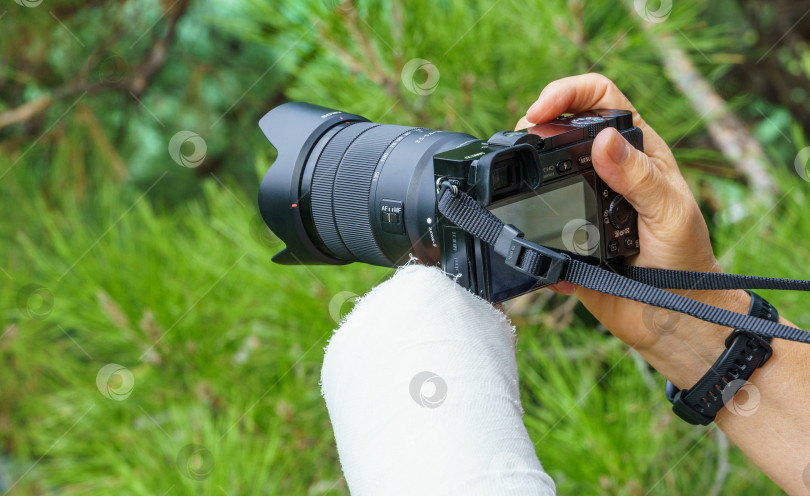 Скачать Фотограф со сломанной рукой в белой гипсовой повязке, держащий фотоаппарат Sony фотосток Ozero