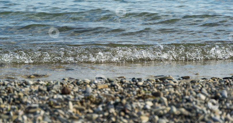 Скачать Прозрачная морская волна накатывает на берег. Выборочный фокус на волне и расфокусированной морской гальке на переднем плане. фотосток Ozero