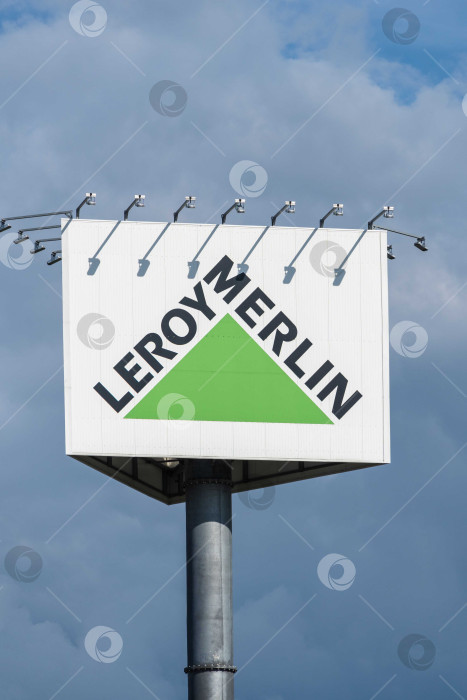 Скачать Рекламный столб перед входом на парковку Leroy Merlin. Название магазина Leroy Merlin по сторонам зеленого треугольника. Рекламный столб на фоне пасмурного весеннего неба. фотосток Ozero