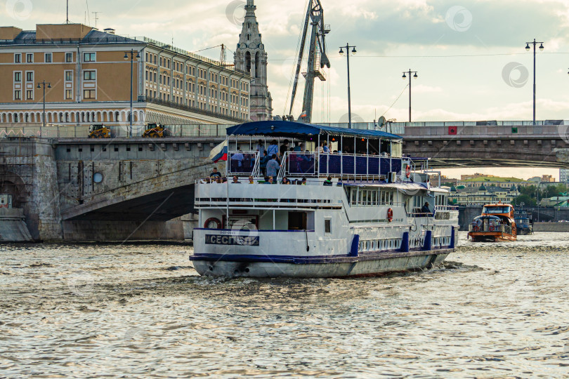 Скачать Ремонт автомобильного моста на Москворецкой набережной. Прогулочный катер с людьми на борту находится под мостом через Москву-реку. Плавучий кран на пирсе. фотосток Ozero